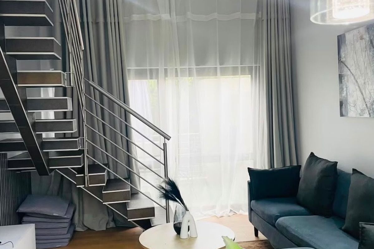 Modern living room featuring a contemporary staircase with metal balustrades, recessed lighting, and light wood-tone flooring.