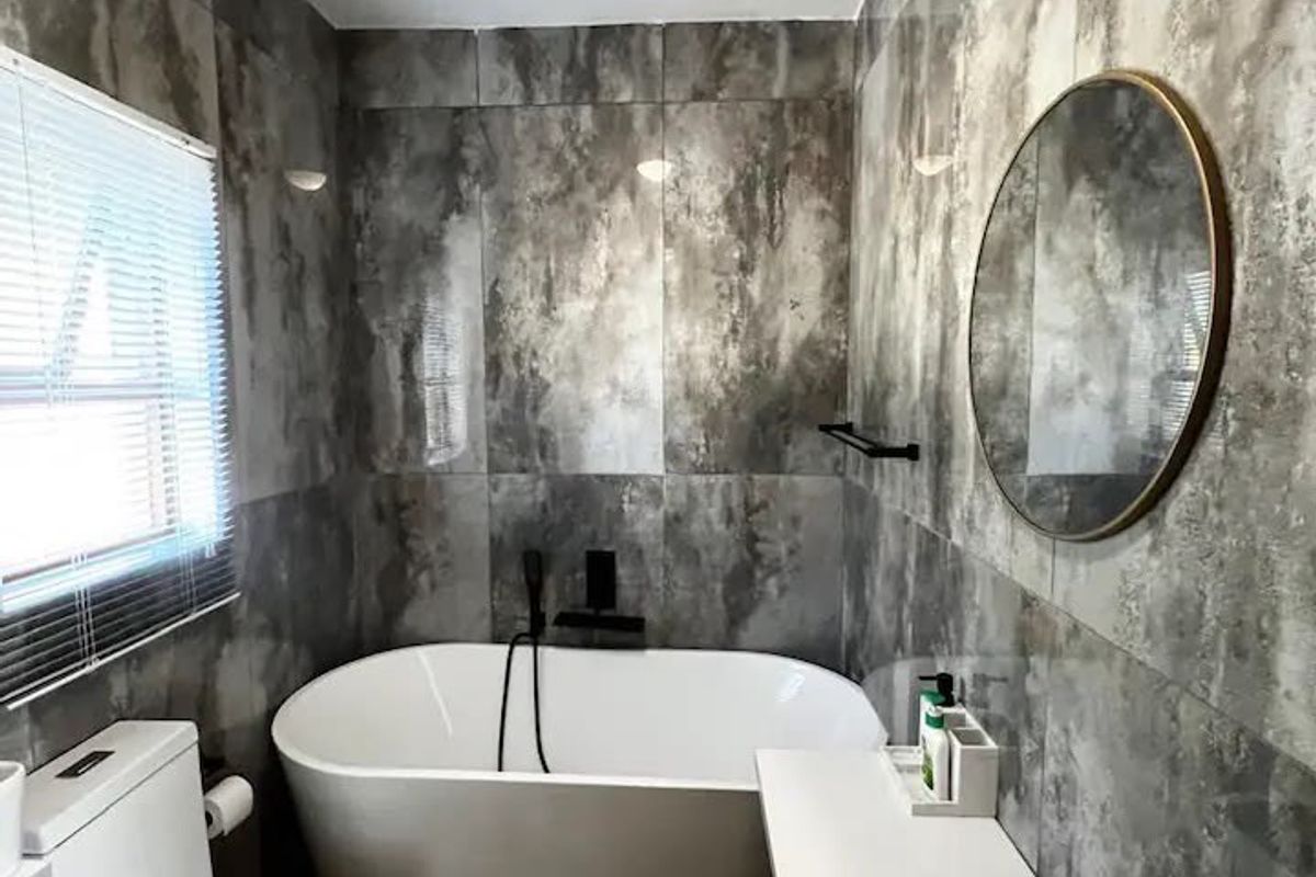 Modern bathroom featuring a freestanding bathtub, wall-mounted toilet, and contemporary grey tiled walls with a sleek vanity unit.