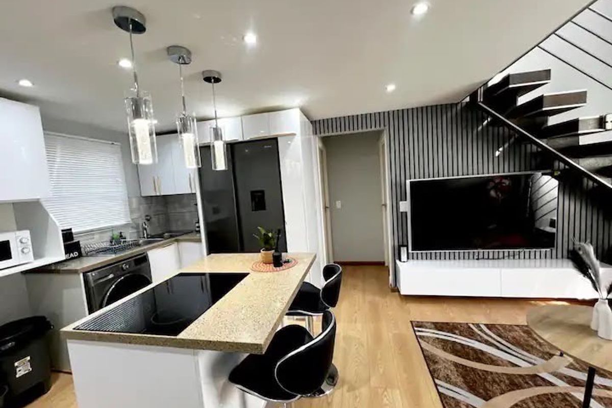 Modern open-plan kitchen and living area featuring a central island with integrated hob, sleek cabinetry, and a contemporary staircase with slatted feature wall.