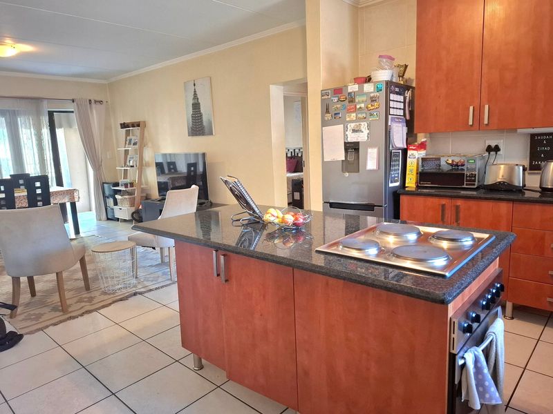 Open-plan living area featuring a kitchen with granite countertops, built-in hob and oven, wooden cabinetry, and tiled flooring leading to a patio.