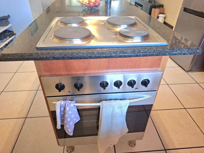 A kitchen island featuring a granite countertop, integrated electric hob, and built-in oven with stainless steel finish.