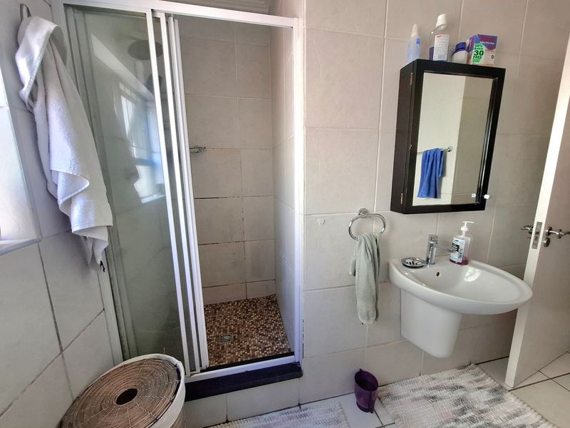 A functional bathroom featuring a shower enclosure with tiled flooring, a pedestal basin, and a wall-mounted mirror cabinet.