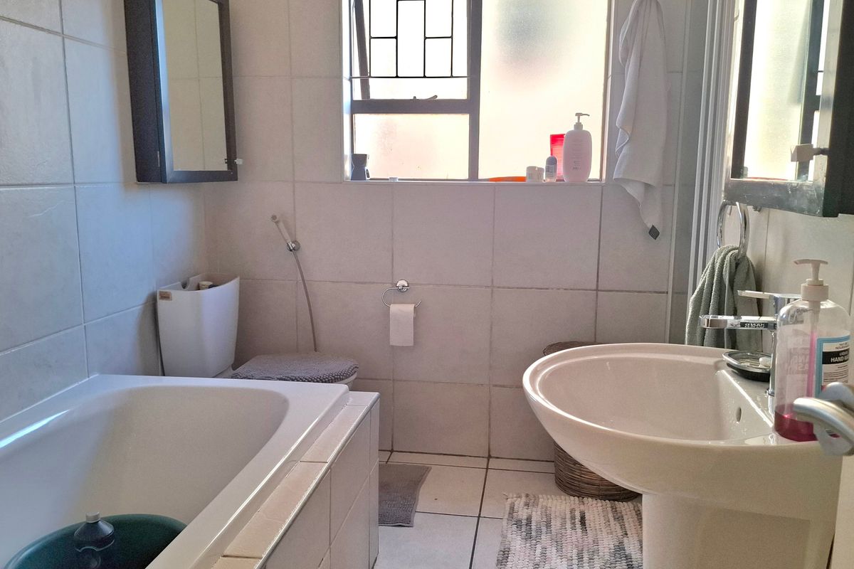 A functional bathroom featuring a pedestal basin, built-in bathtub, and toilet with tiled finishes throughout.