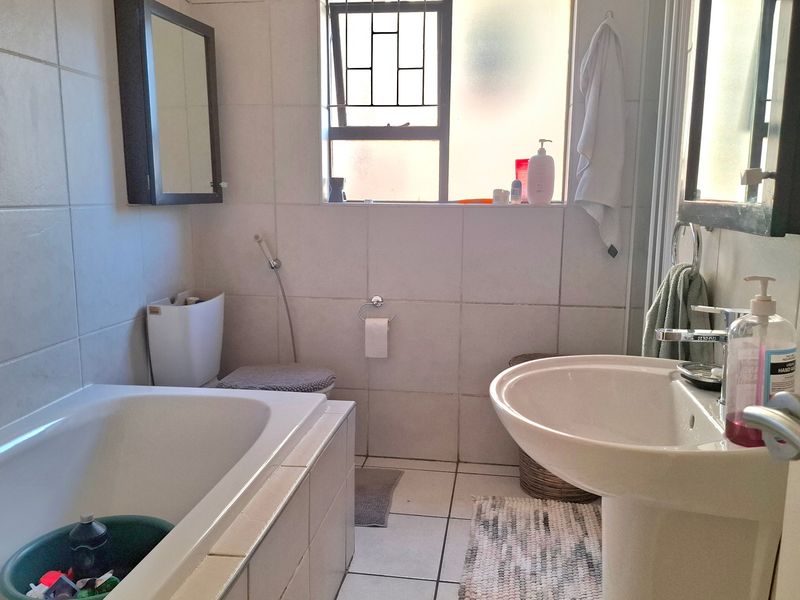 A functional bathroom featuring a pedestal basin, built-in bathtub, and toilet with tiled finishes throughout.