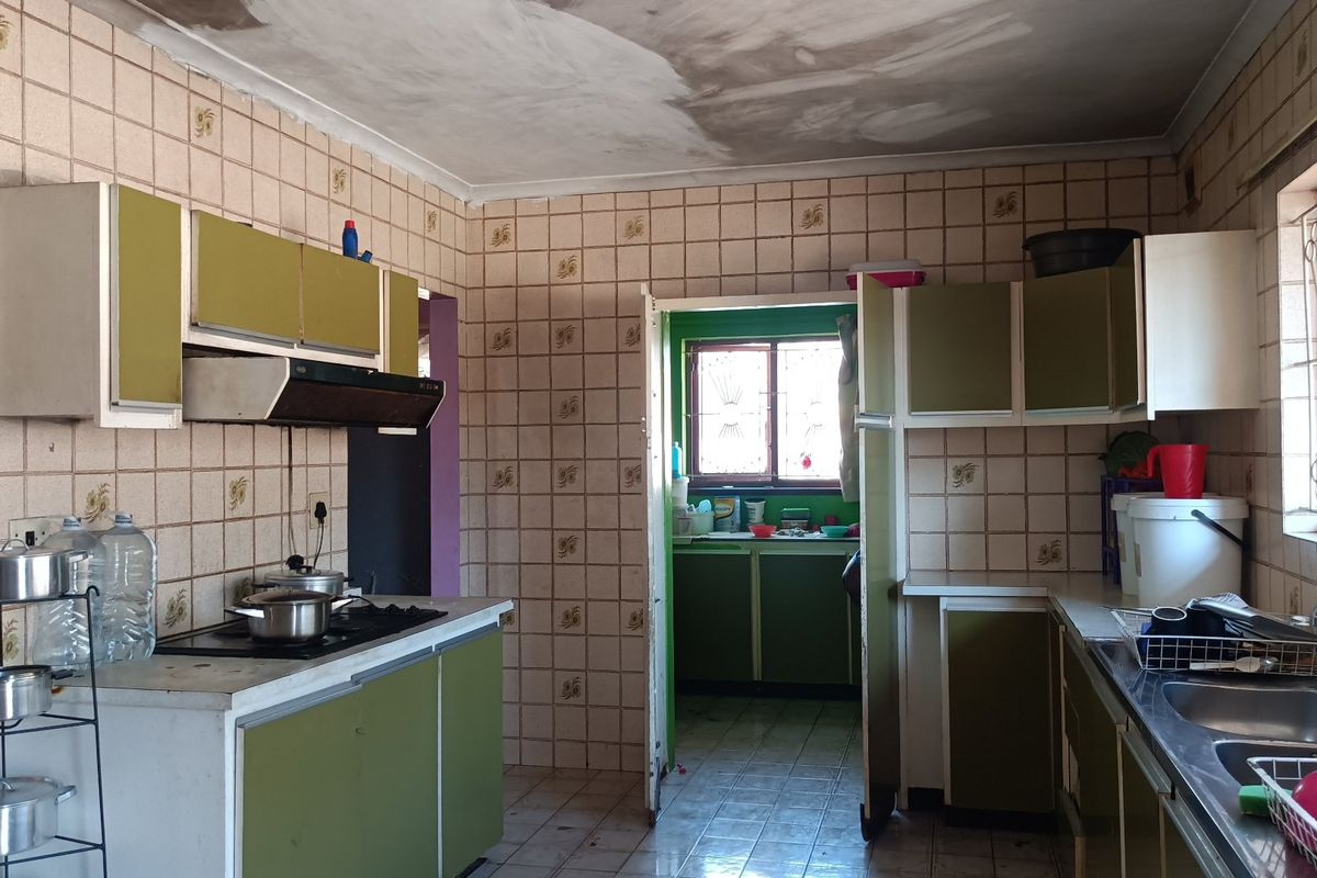 A dated kitchen featuring original cabinetry, gas hob, and tiled finishes, currently showing signs of ceiling water damage and requiring modernization.