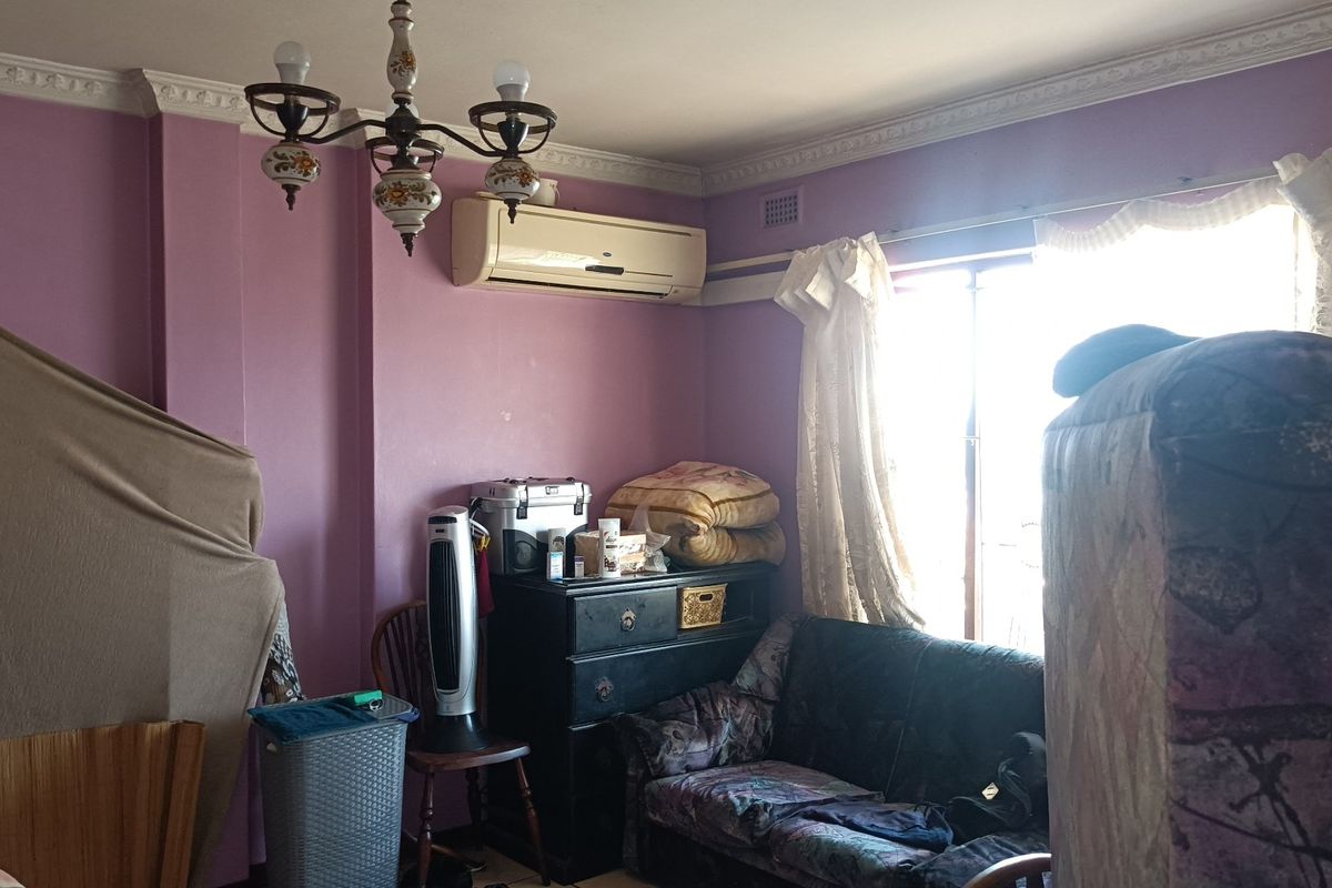 A living room featuring decorative ceiling cornices, a central chandelier, and a wall-mounted split-system air conditioner.