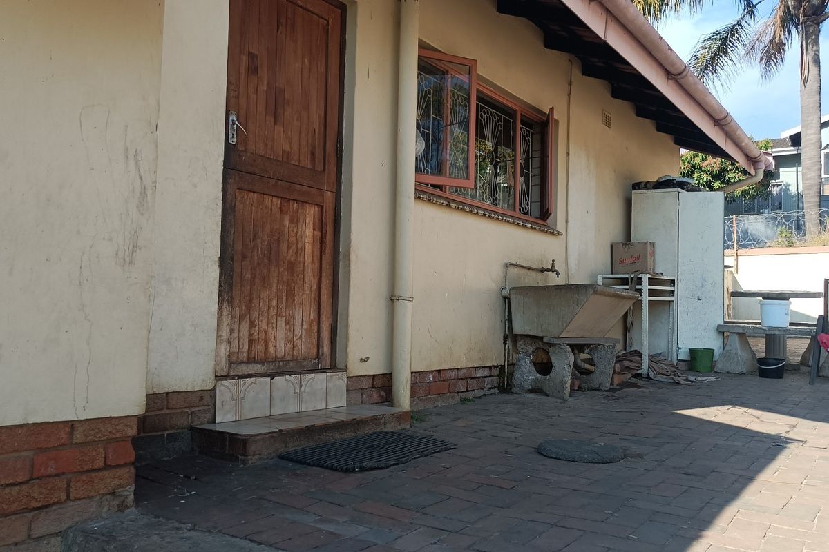 Rear exterior view of the property featuring brick paving, a concrete wash basin, and a timber door with security gate.