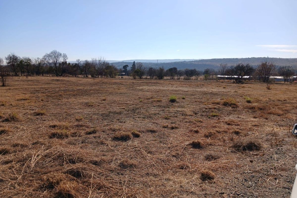 An expansive view of the open farm landscape featuring dry grassland and distant hills under a clear blue sky.