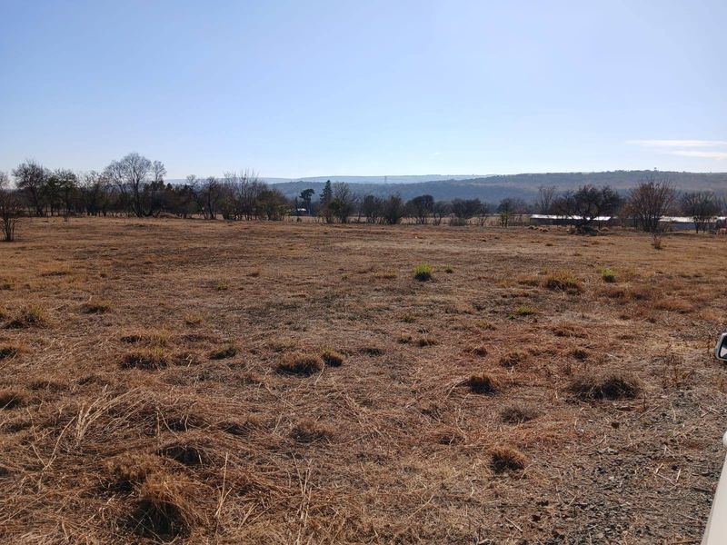 An expansive view of the open farm landscape featuring dry grassland and distant hills under a clear blue sky.