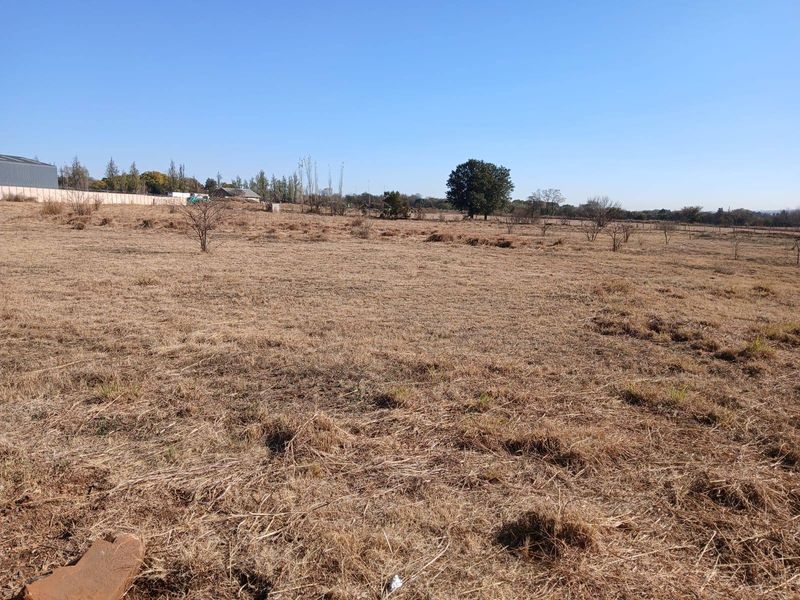 A wide-angle view of an expansive, undeveloped farm field with dry grass and distant perimeter fencing under a clear blue sky.