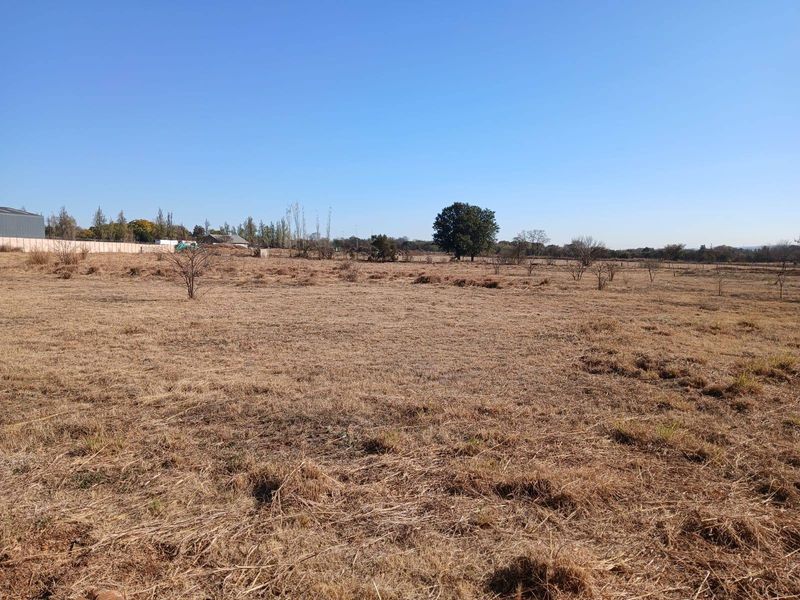 Expansive open farm land with dry grass, scattered trees, and perimeter fencing, offering significant potential for agricultural or development use.