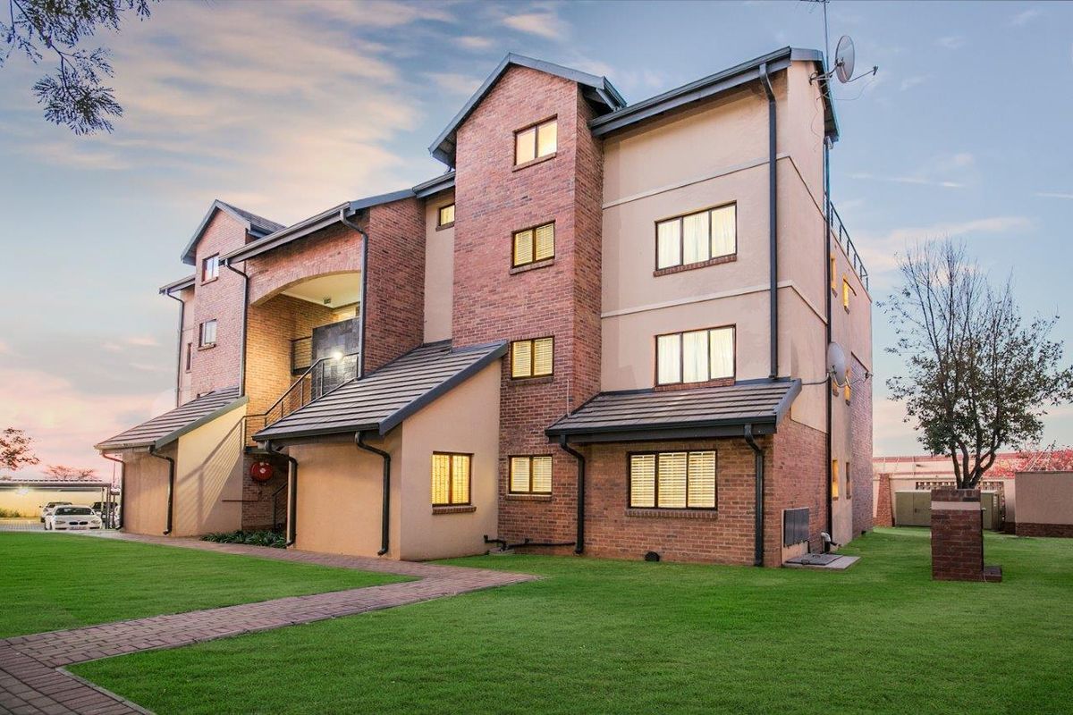 A well-maintained multi-story apartment building featuring a brick and plaster facade, tiled roof, and neatly landscaped surrounding lawn with paved pathways.