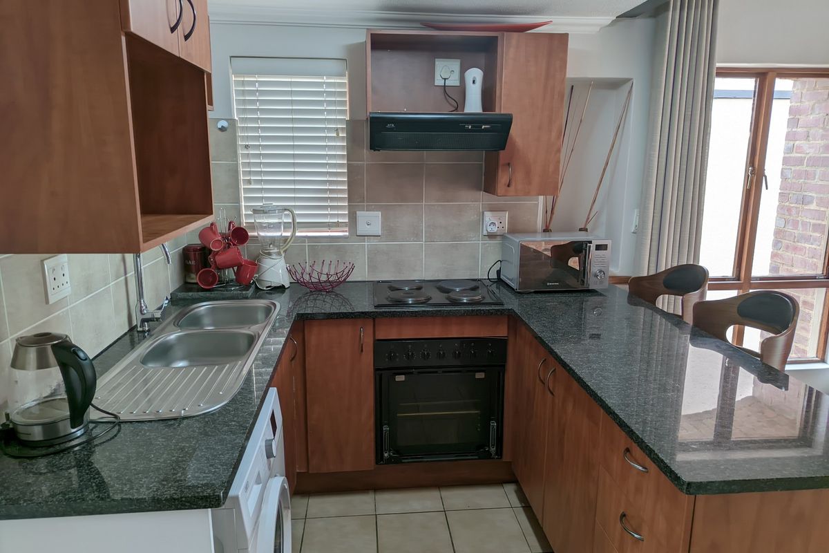 A functional U-shaped kitchen featuring wood-finish cabinetry, granite countertops, a built-in oven and hob, and tiled flooring with direct access to an outdoor area.