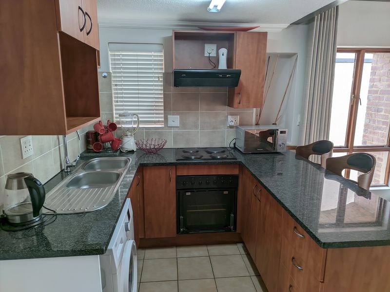 A functional U-shaped kitchen featuring wood-finish cabinetry, granite countertops, a built-in oven and hob, and tiled flooring with direct access to an outdoor area.