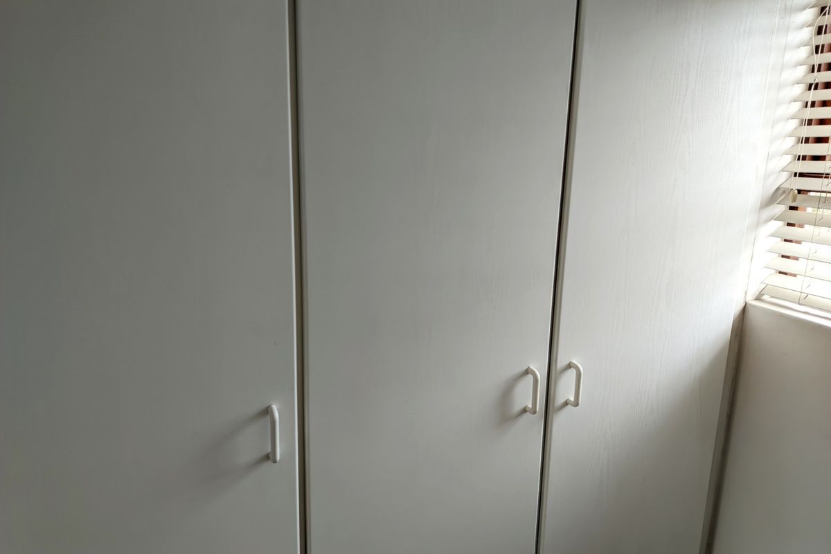 A bedroom interior featuring white built-in cupboards and venetian blinds on the window.