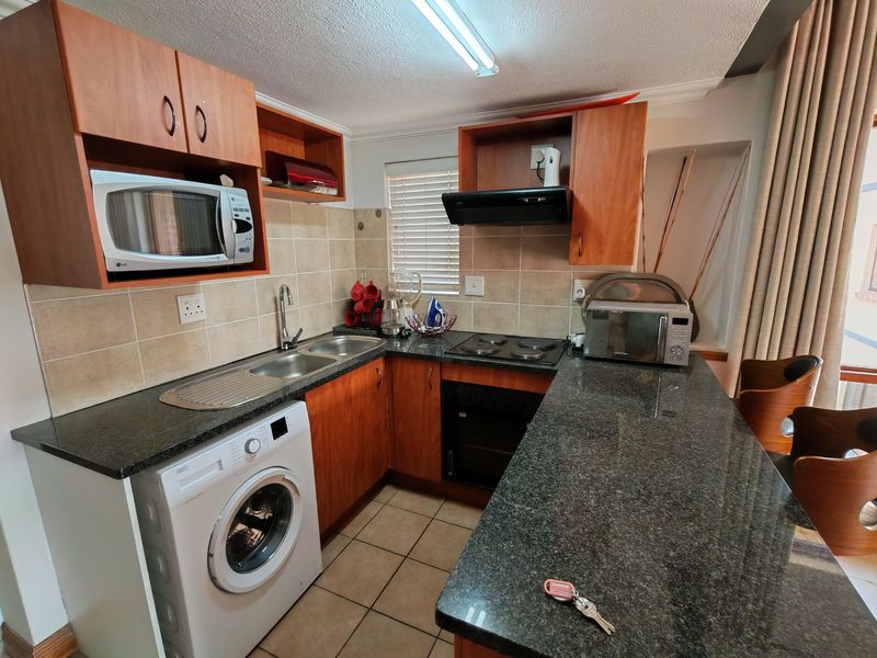 Compact kitchen featuring granite countertops, built-in oven, electric hob, extractor fan, and integrated laundry plumbing, offering a functional layout for apartment living.
