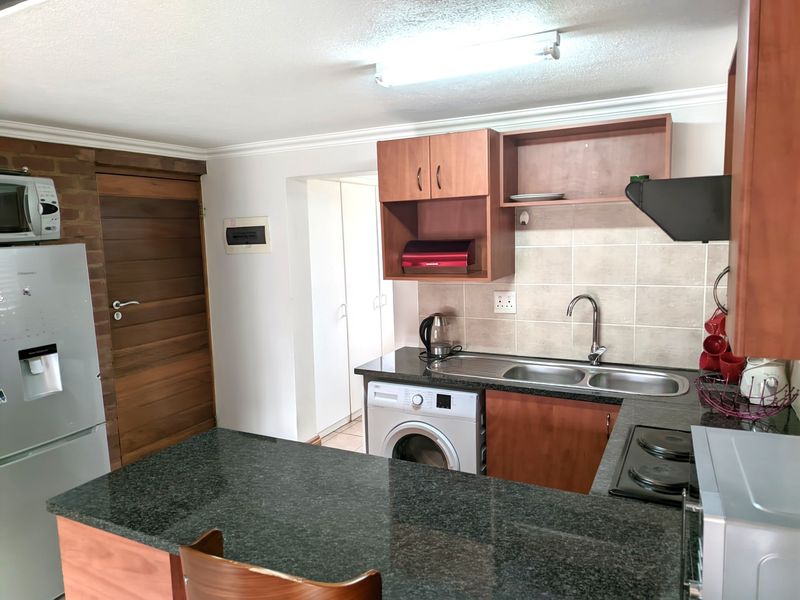 A functional kitchen featuring granite countertops, built-in wooden cabinetry, a stainless steel double sink, and a built-in hob with an extractor fan.