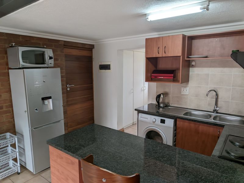 Functional kitchen featuring granite countertops, built-in cabinetry, a stainless steel sink, and a brick feature wall, offering a practical layout for daily use.