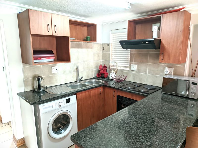Compact kitchen featuring laminate cabinetry, granite countertops, a built-in oven with hob, extractor fan, and dedicated space for a washing machine.