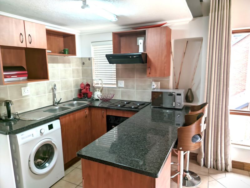 A functional kitchen featuring laminate cabinetry, granite countertops, a built-in hob, oven, extractor fan, and integrated space for a washing machine.