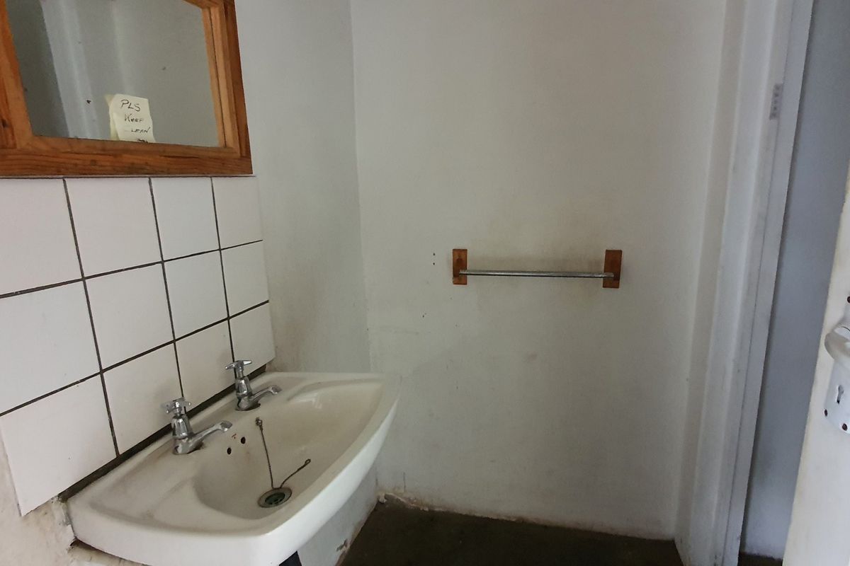 A small, dated bathroom featuring a pedestal basin with tiled splashback and a wall-mounted mirror, requiring cosmetic updates and refurbishment.