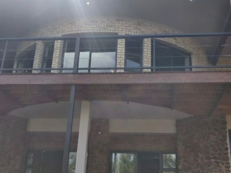 A spacious elevated balcony featuring timber decking, metal railings, and brick masonry, providing an expansive outdoor area connected to the upper level of the home.