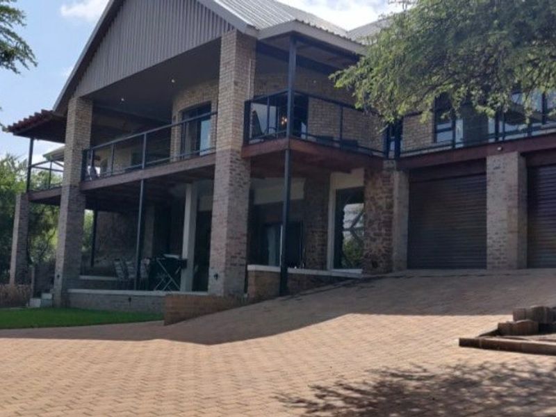 A multi-level brick house featuring a spacious paved driveway, double garage, and an expansive upper-level balcony with glass balustrades.