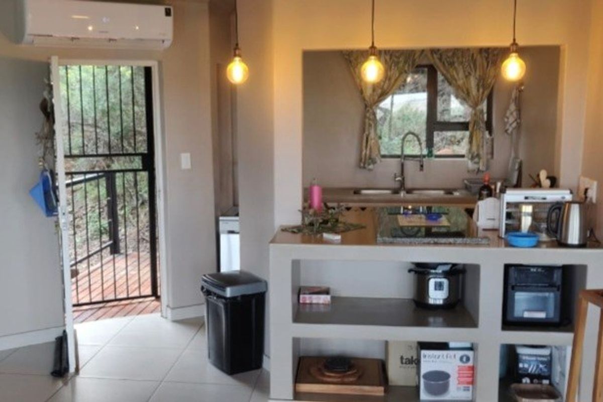 A compact kitchen area featuring built-in cabinetry, a sink, and pendant lighting, with direct access to an outdoor deck through a security gate.