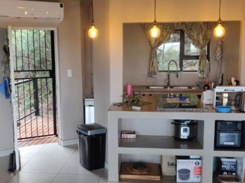A compact kitchen area featuring built-in cabinetry, a sink, and pendant lighting, with direct access to an outdoor deck through a security gate.