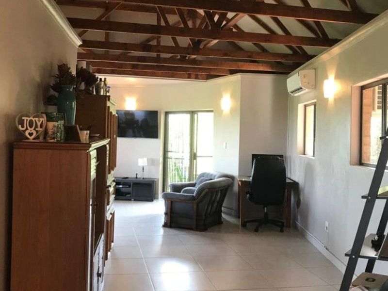 Spacious living area featuring high vaulted ceilings with exposed timber trusses, tiled flooring, and a wall-mounted air conditioning unit.
