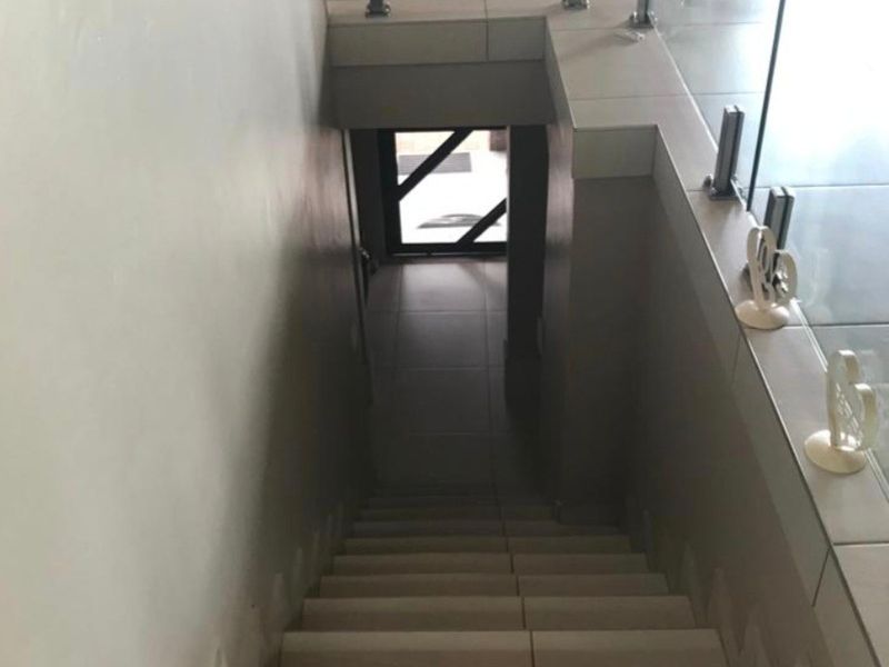 A tiled staircase featuring a modern glass balustrade with stainless steel spigots, leading to a lower level entrance.