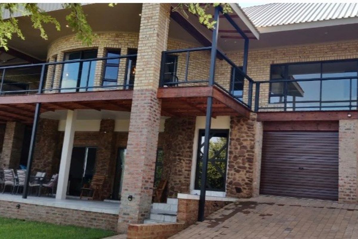 Rear elevation of a multi-level house featuring face brick and stone cladding, a raised timber deck with metal balustrades, and a double garage.