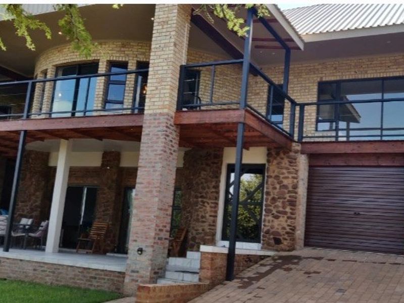Rear elevation of a multi-level house featuring face brick and stone cladding, a raised timber deck with metal balustrades, and a double garage.