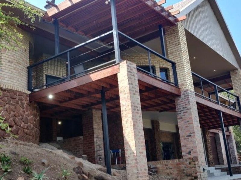 Rear elevation of a multi-level house featuring a large timber deck with a pergola, brick pillars, and stone cladding accents.