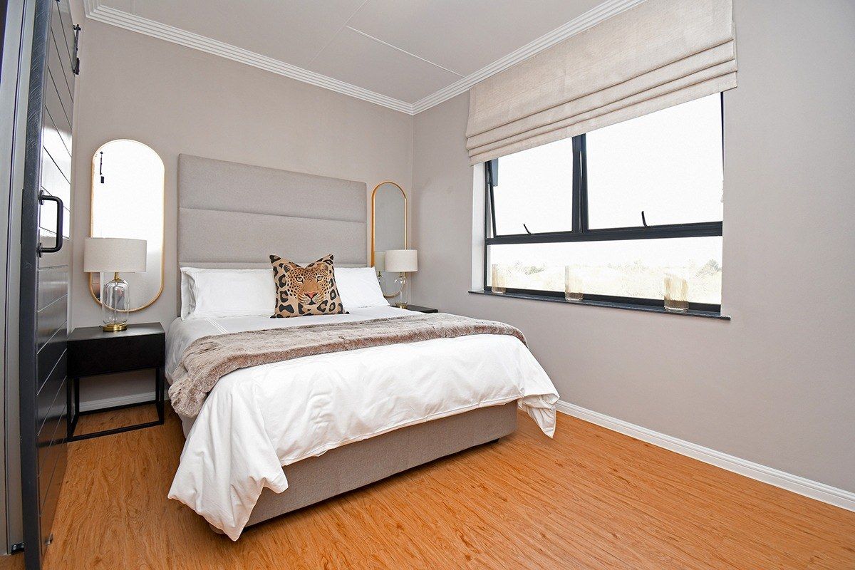 A well-maintained bedroom featuring light-toned laminate flooring, neutral wall finishes, and a large window with a fitted roman blind.