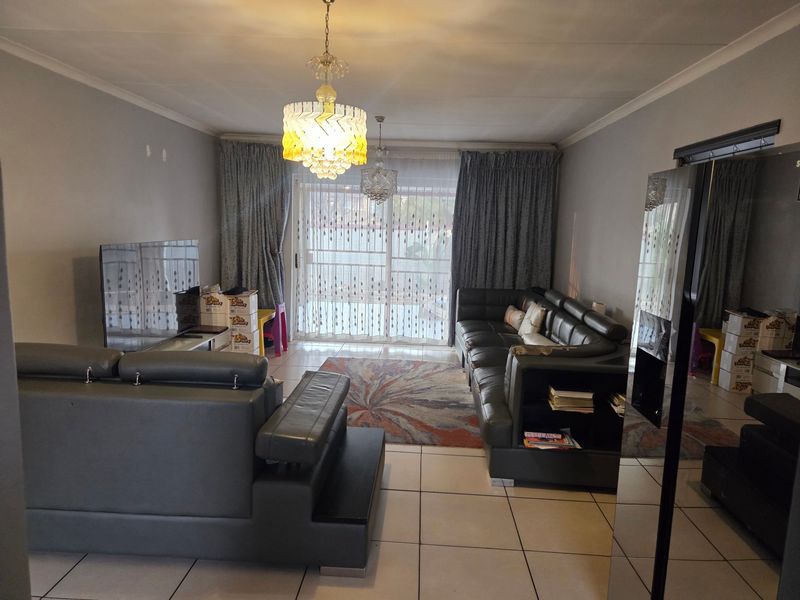 A spacious living room featuring tiled flooring, decorative ceiling light fixtures, and a large sliding glass door providing access to the exterior.