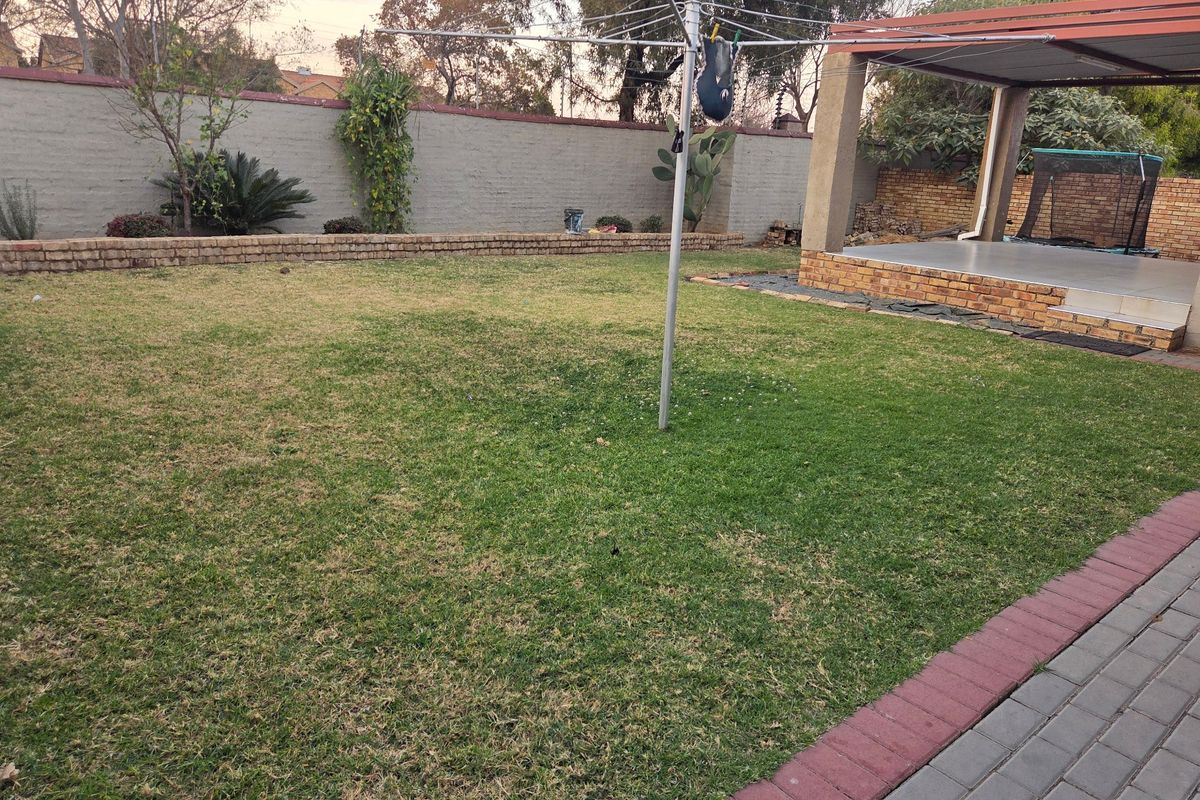 A spacious rear garden featuring a lawn, a covered patio area, and a brick boundary wall.