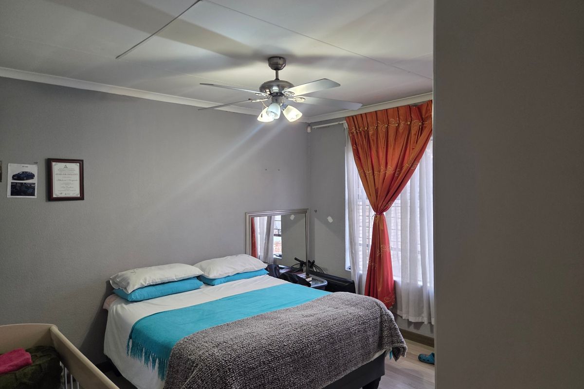 A functional bedroom featuring laminate flooring, a ceiling fan, and window security bars, providing a comfortable and secure living space.