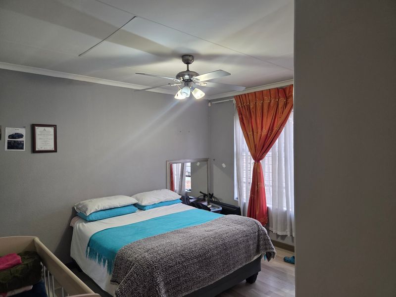 A functional bedroom featuring laminate flooring, a ceiling fan, and window security bars, providing a comfortable and secure living space.