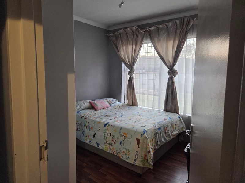 A bedroom featuring laminate flooring, security bars on the window, and neutral wall finishes.