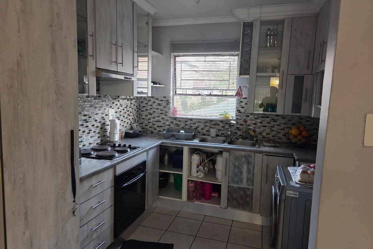 Compact kitchen featuring wood-look cabinetry, mosaic tile backsplash, integrated oven and hob, and double sink with tiled flooring.
