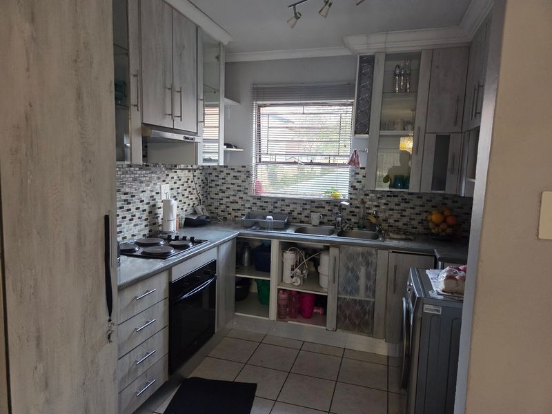 Compact kitchen featuring wood-look cabinetry, mosaic tile backsplash, integrated oven and hob, and double sink with tiled flooring.