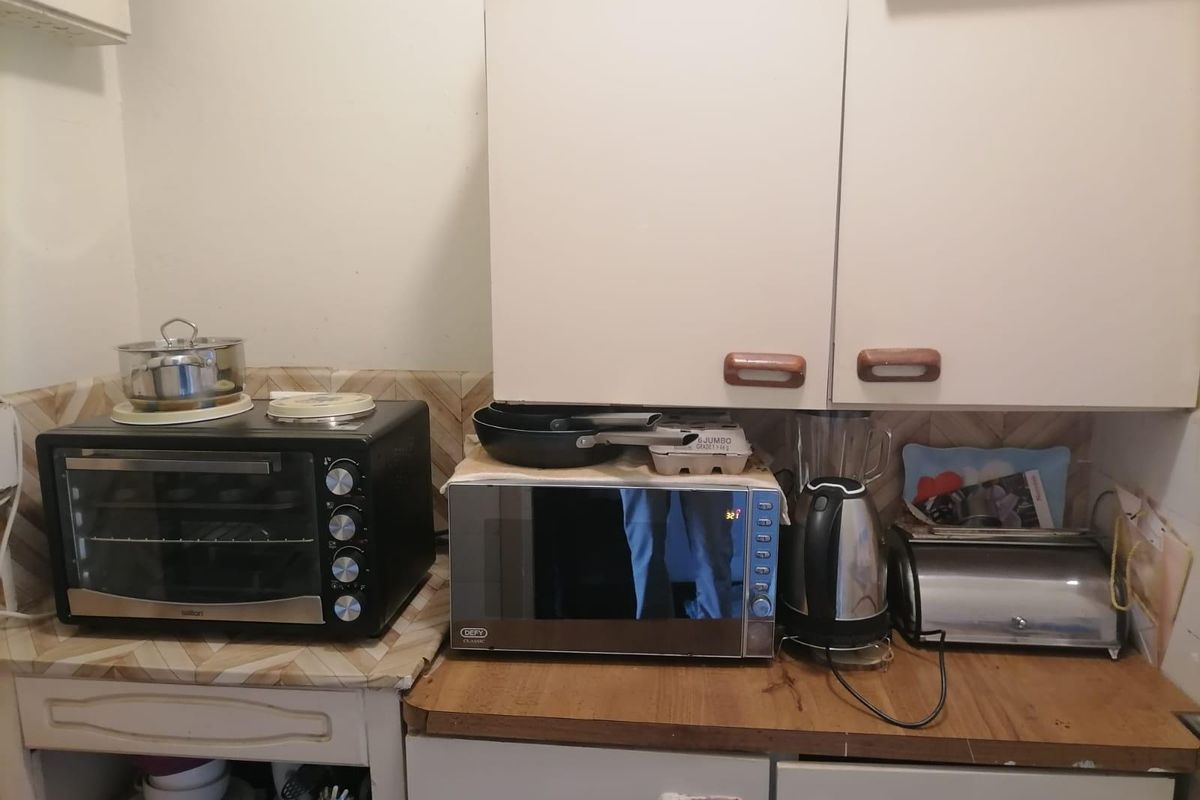 A compact kitchen area featuring dated cabinetry, laminate countertops, and a tiled backsplash, providing a functional but aged workspace.
