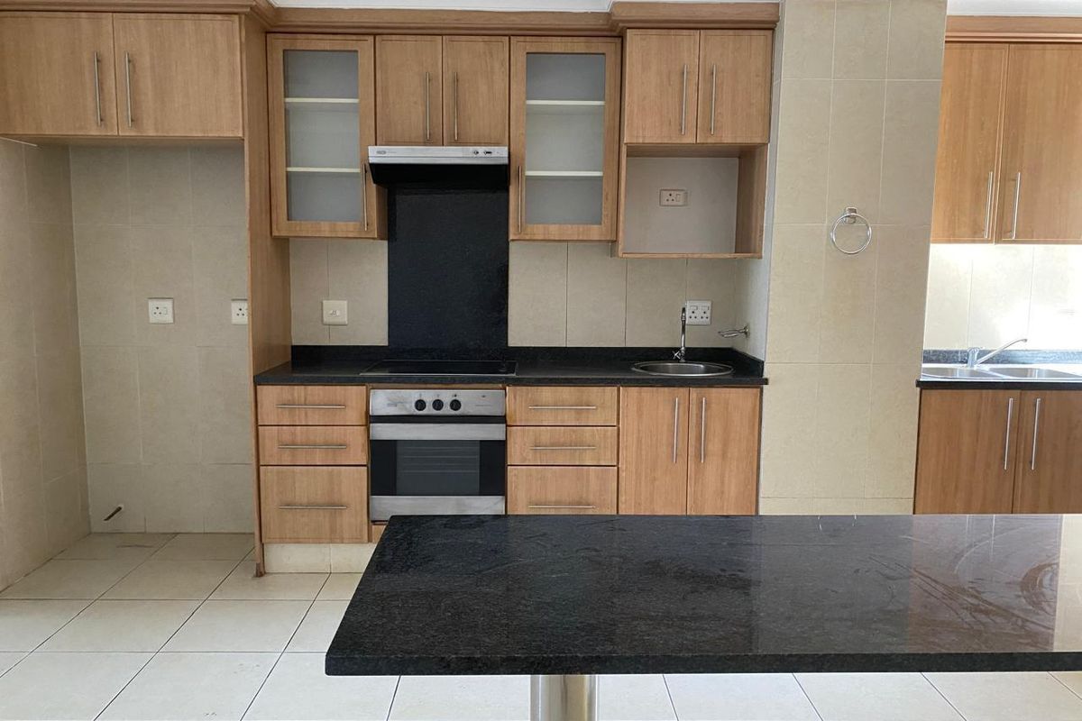 A clean, functional kitchen featuring light wood cabinetry, dark granite countertops, built-in oven and hob, and a convenient breakfast bar island.
