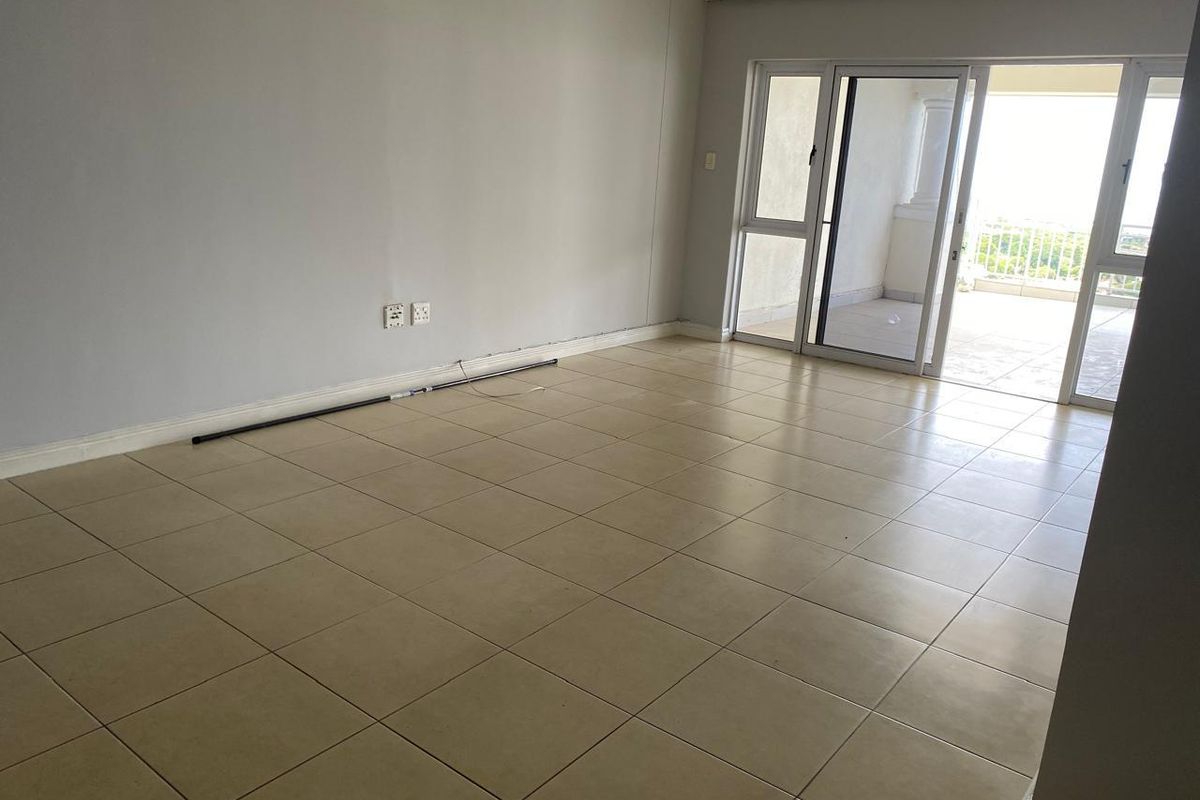 An empty, open-plan living area featuring neutral tiled flooring and large sliding glass doors that provide access to an outdoor balcony space.
