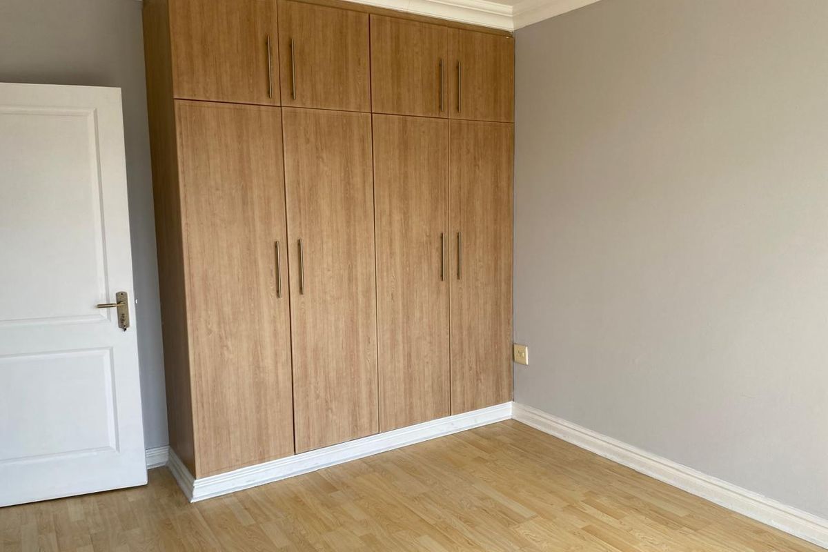 A clean, empty bedroom featuring modern wood-finish built-in cupboards, laminate flooring, and neutral wall tones.