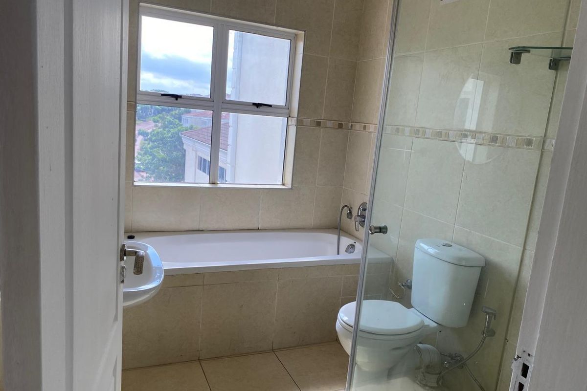 A clean, functional bathroom featuring a bathtub, a separate glass-enclosed shower area, and neutral wall and floor tiling.