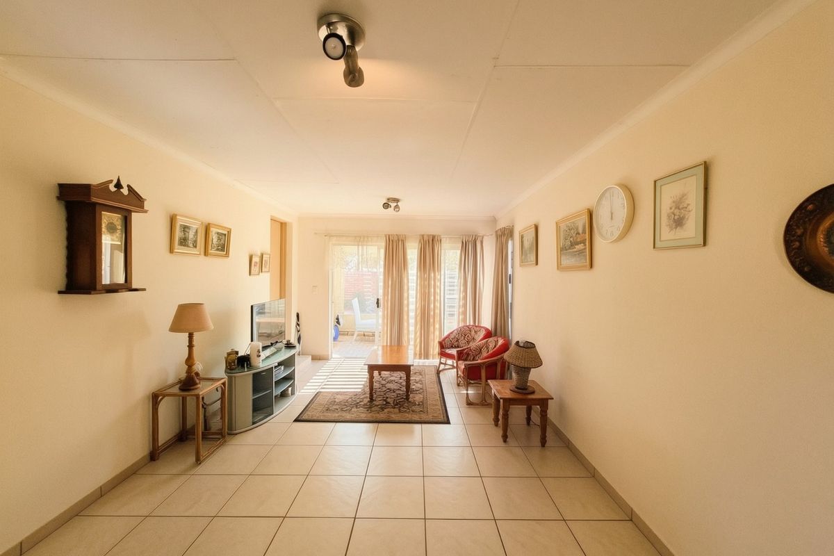 A bright living room featuring neutral tiled flooring and a sliding glass door providing access to the outdoor patio area.
