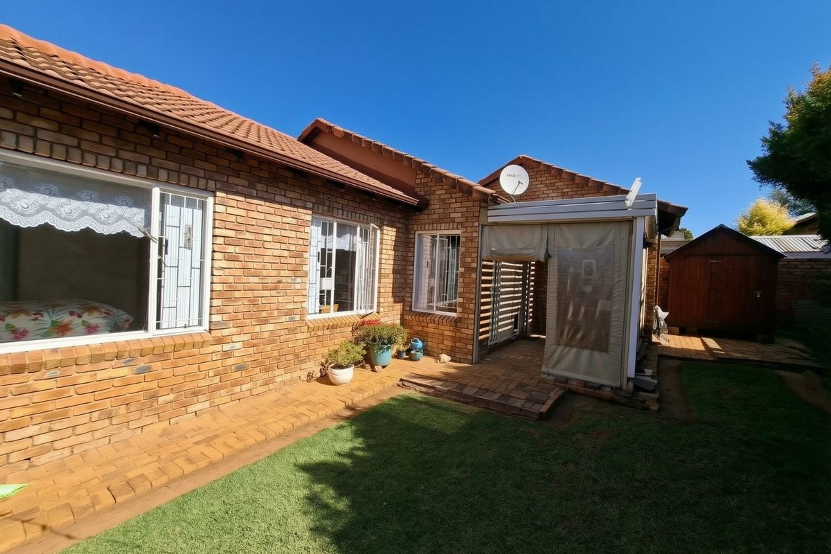 Rear view of the townhouse featuring a face brick facade, tiled roof, and a covered patio area leading onto a small garden.