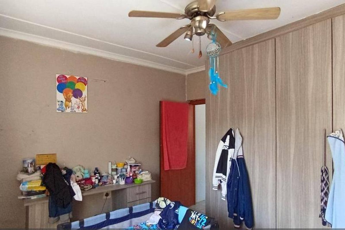 A bedroom featuring built-in wooden cupboards, a ceiling fan, and an air conditioning unit, providing functional storage and climate control.